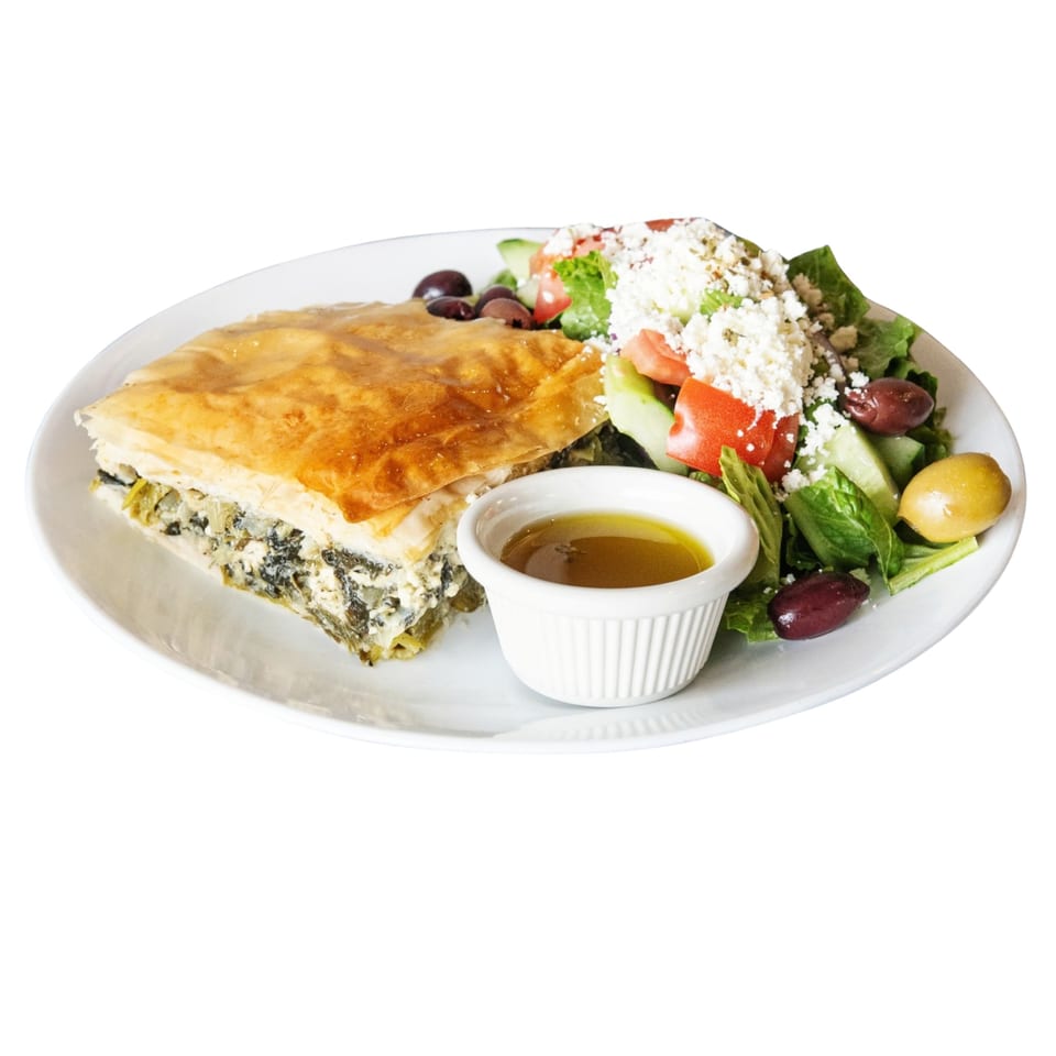 A slice of spanakopita with a side of Greek salad, olives, and dressing on a white plate.