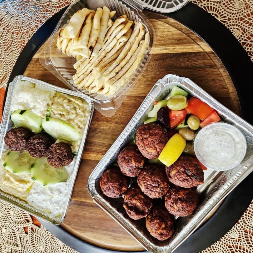 Mediterranean takeout meal with falafel, hummus, pita bread, salad, and sauce on a wooden tray.
