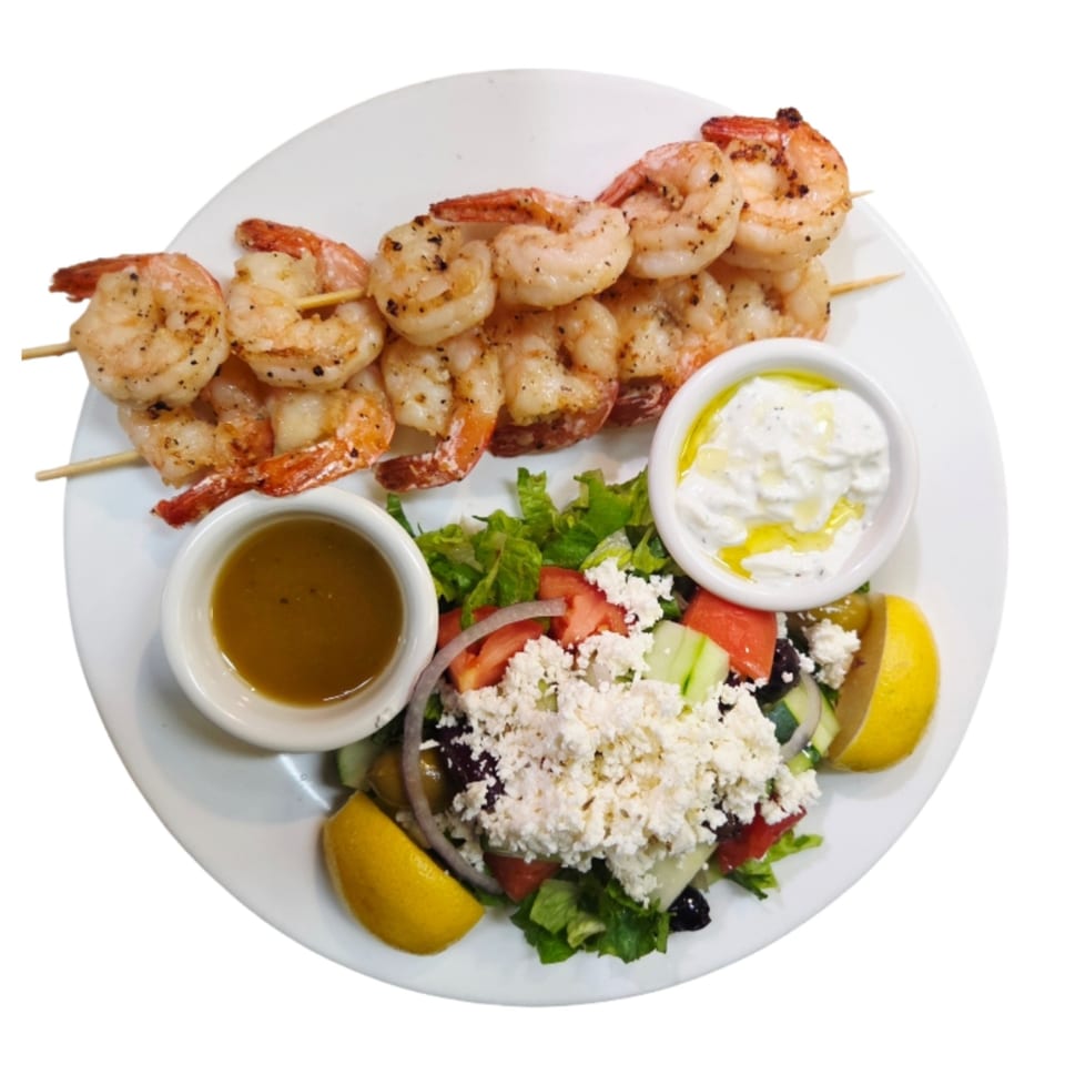 Grilled shrimp skewers, a Greek salad with feta, and two dipping sauces on a white plate.